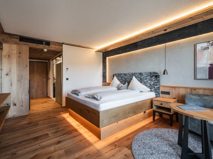 Modernes Hotelzimmer mit Holzmöbeln, Doppelbett, Akzentbeleuchtung und gemütlicher Sitzecke